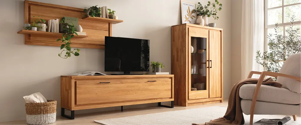 Wohnzimmer mit Wohnwand aus Massivholz, Lowboard, Vitrine und Wandregal in Eiche Natur, kombiniert mit Fernseher und dekorativen Pflanzen für eine moderne und wohnliche Einrichtung.